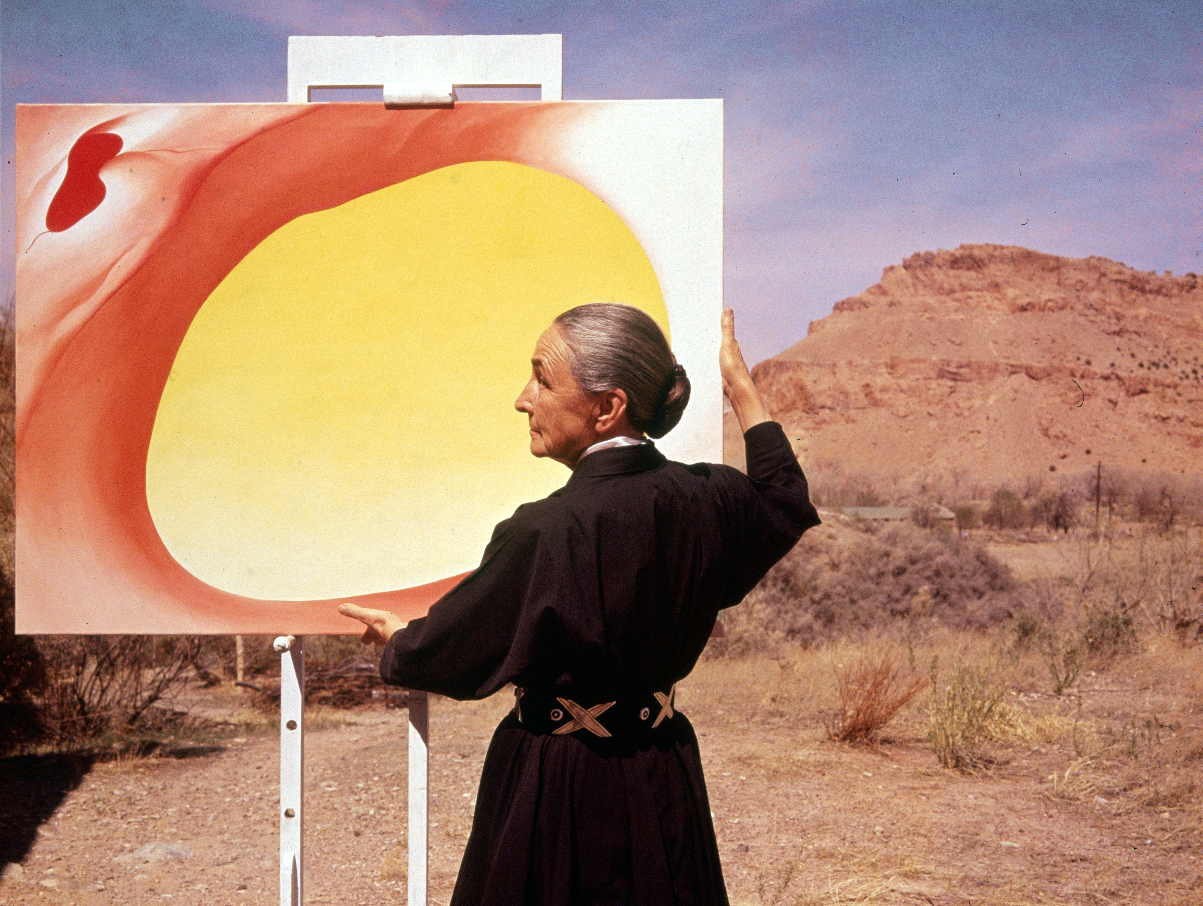 American artist Georgia O’Keeffe (1887 - 1986) stands at an easel outdoors, adjusting a canvas from her “Pelvis Series- Red With Yellow,” Albuquerque, New Mexico, 1960